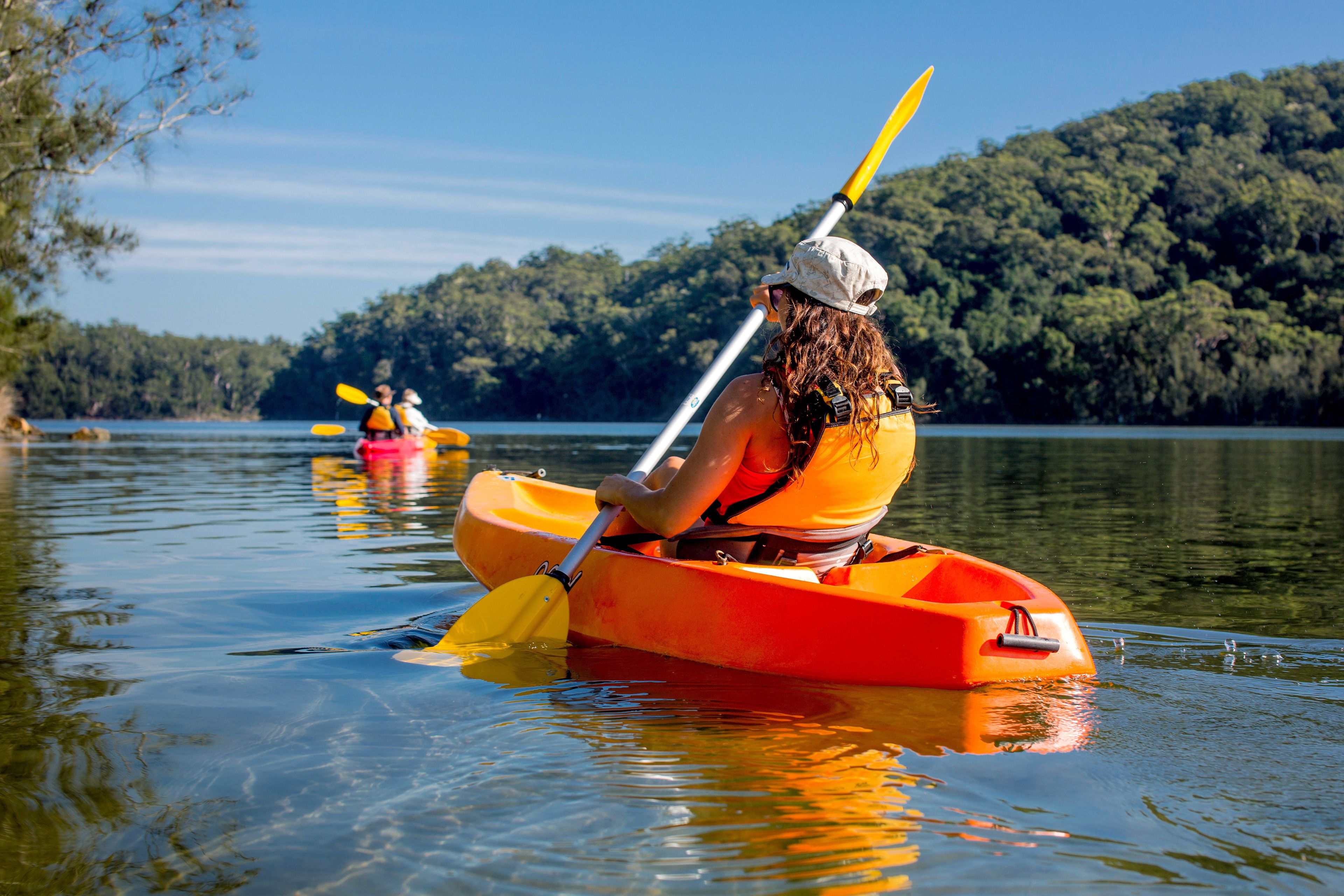 A person kayaking on a calm lake with a forested shoreline in the background.