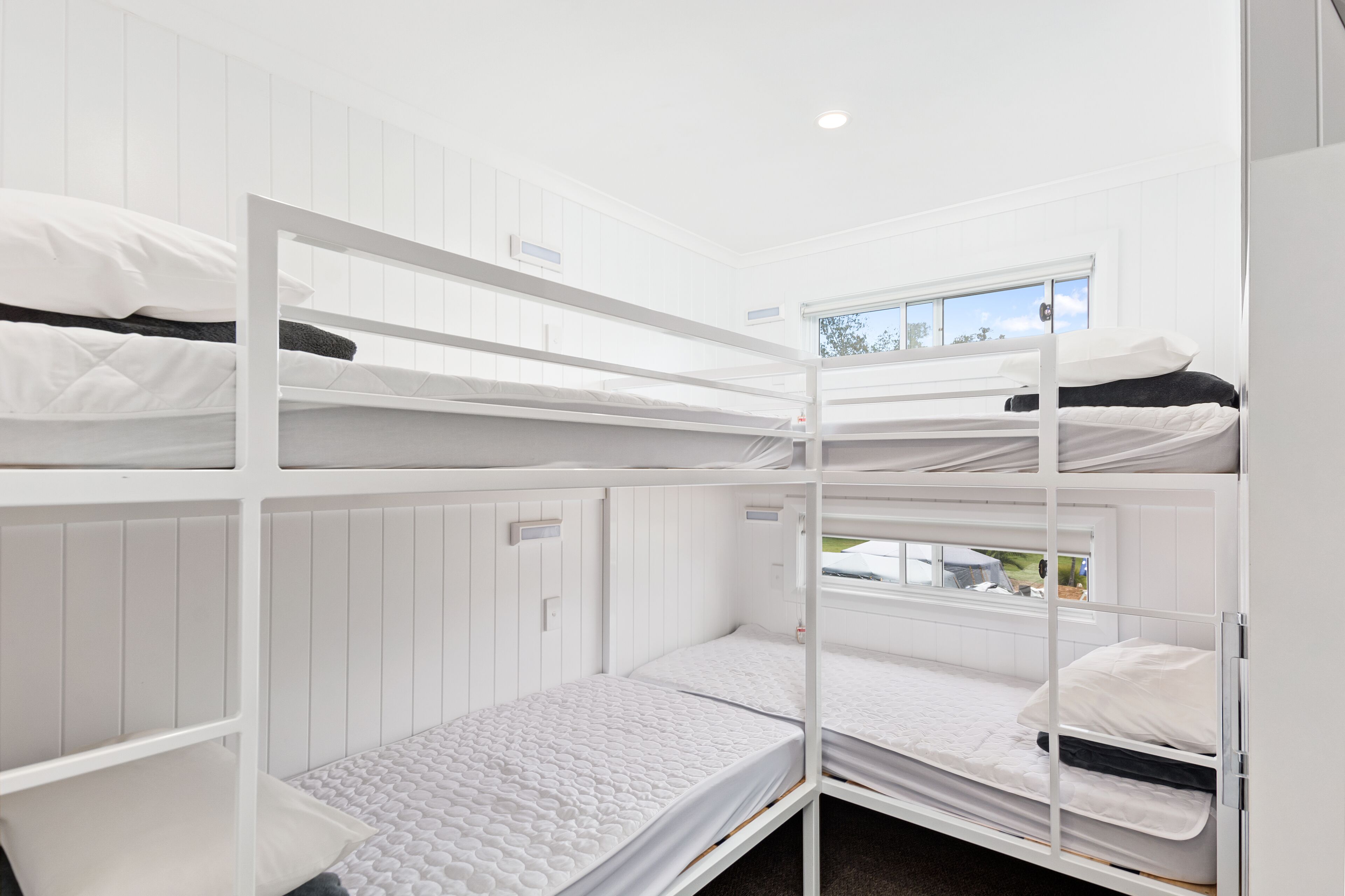 A bunk bed room with white bedding and a window with a view of the outdoors.