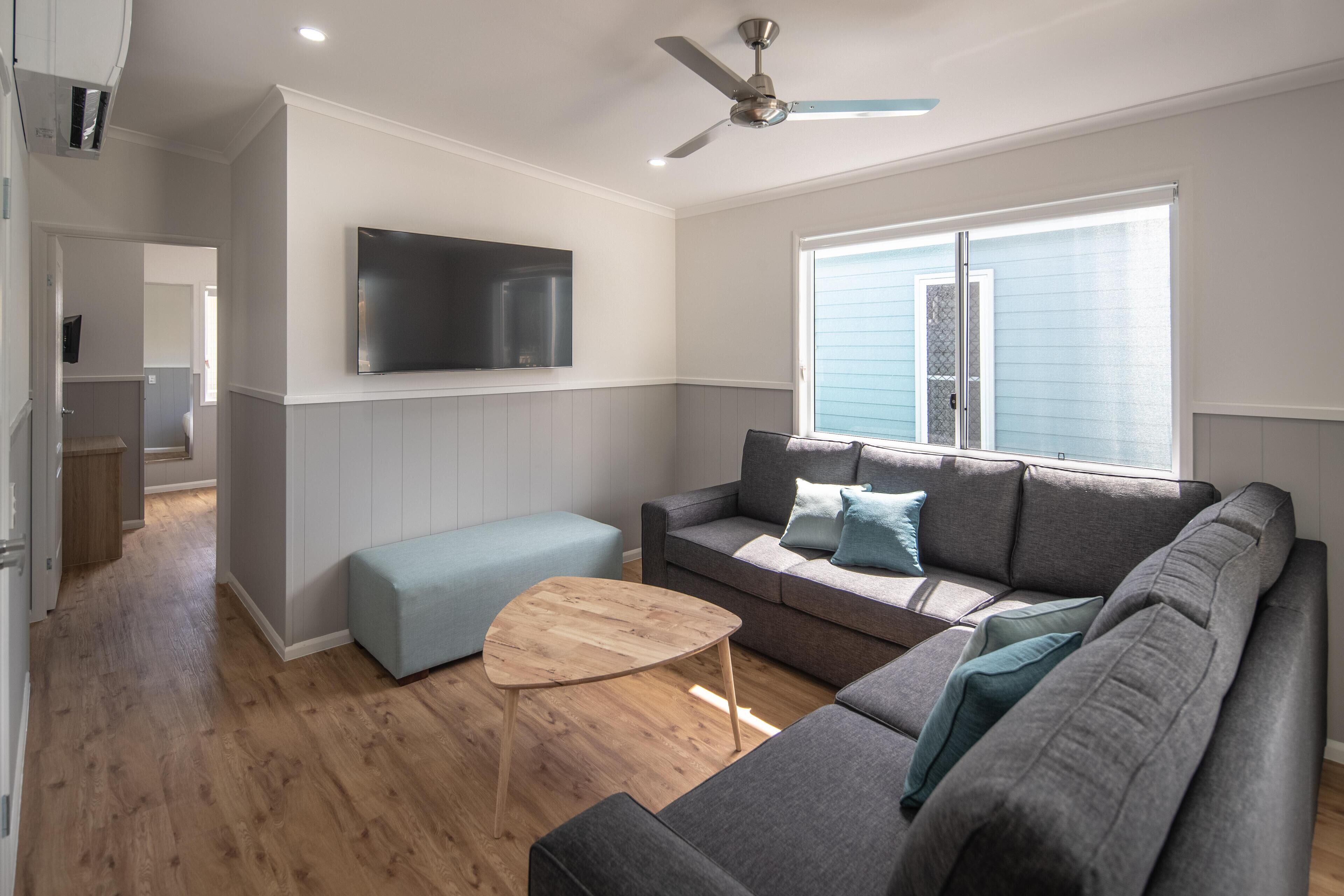 A modern living room with a grey sofa, a wooden coffee table, and a flat-screen TV mounted on the wall.