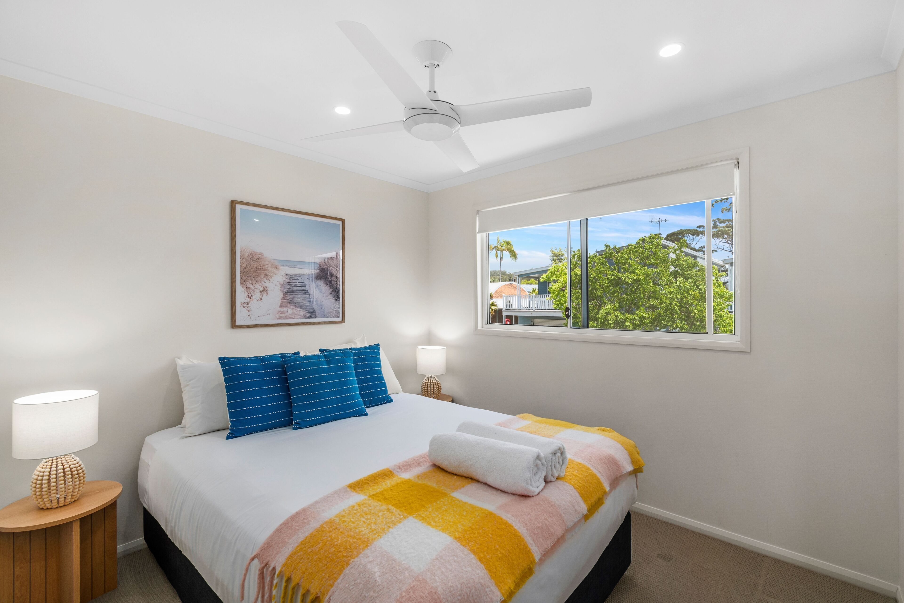 A hotel room with a bed, a ceiling fan, a window with a view, and a framed picture on the wall.