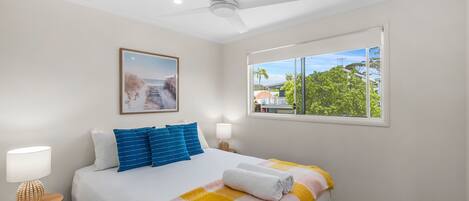 A hotel room with a bed, a ceiling fan, a window with a view, and a framed picture on the wall.