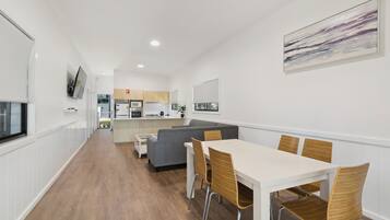 A modern kitchen with white cabinets, a grey sofa, and a dining area with a white table and wooden chairs.