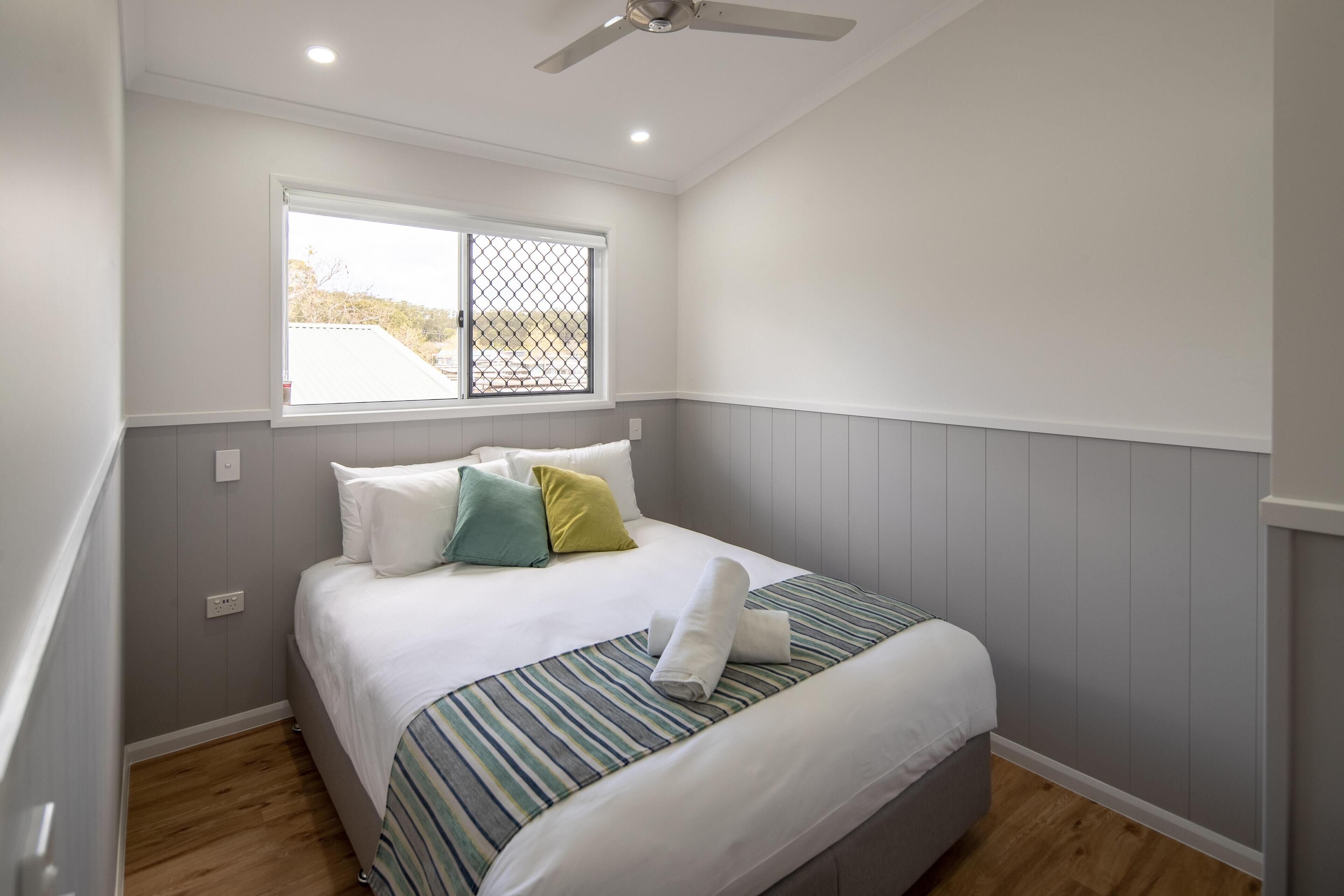 A bedroom with a bed, pillows, a window, and a ceiling fan.