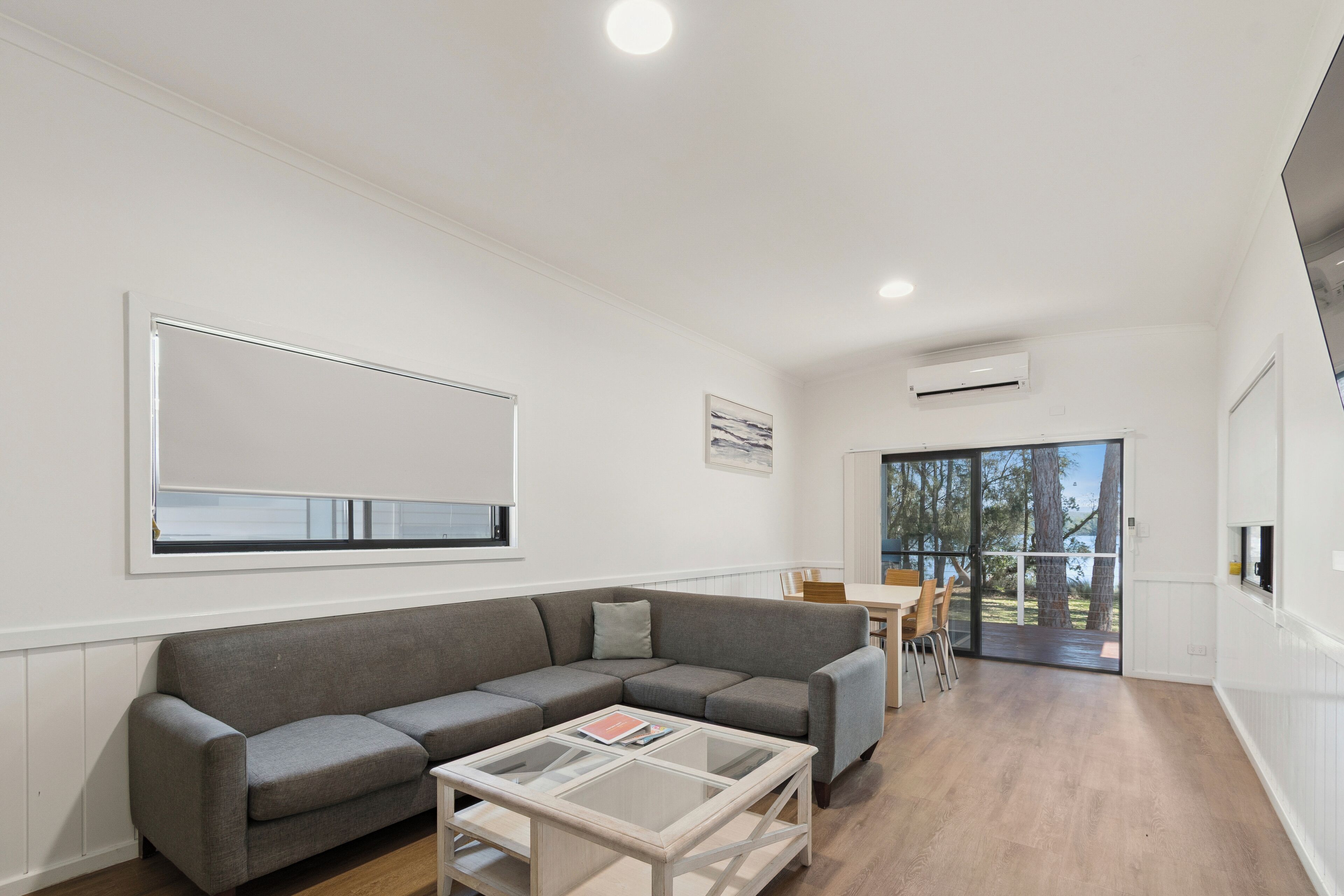 A modern living room with a grey sectional sofa, a glass coffee table, and a dining area with a table and chairs.