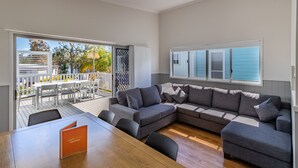 A modern living room with a sectional sofa, a dining table, and a view of an outdoor deck.