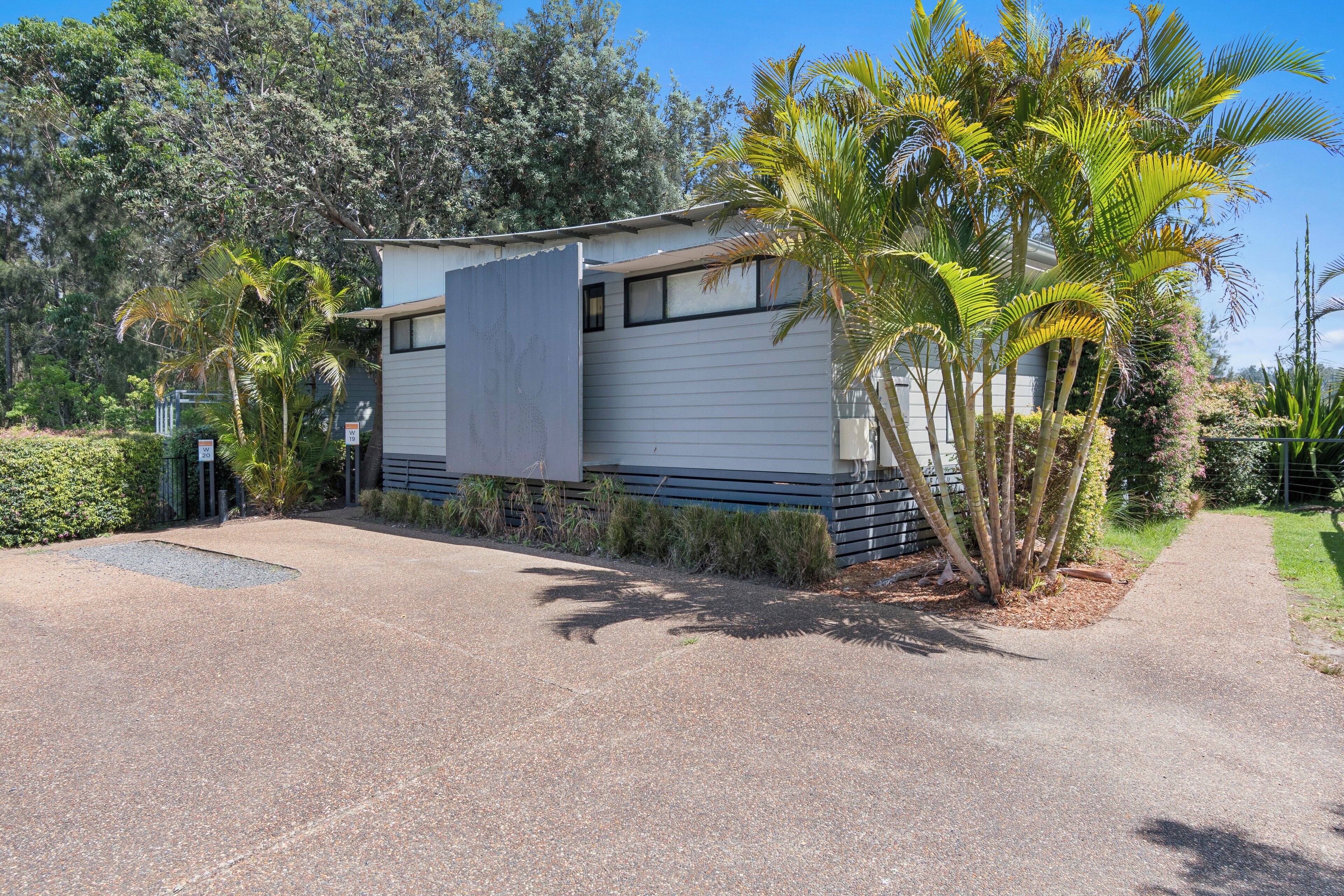 A modern house with a covered driveway, surrounded by lush greenery and palm trees.