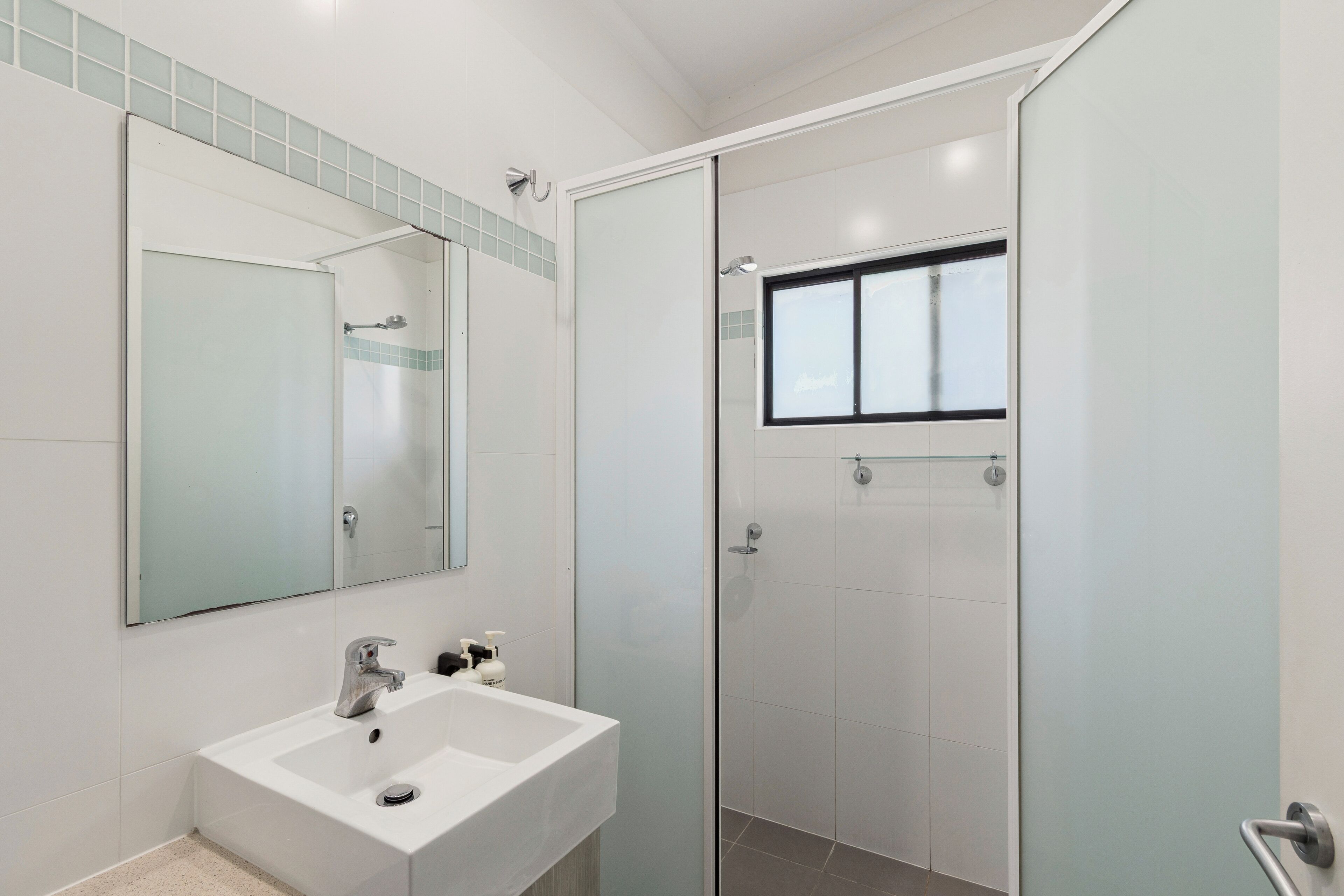 Een moderne badkamer met een witte wastafel, een spiegel en een douche met glazen wanden.