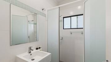 Un baño moderno con un lavamanos blanco, un espejo y una ducha con mampara de vidrio.