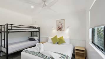 Hotelkamer met een stapelbed, een eenpersoonsbed, een plafondventilator, een nachtkastje, een raam met uitzicht en een lijst met kunstwerk aan de muur.