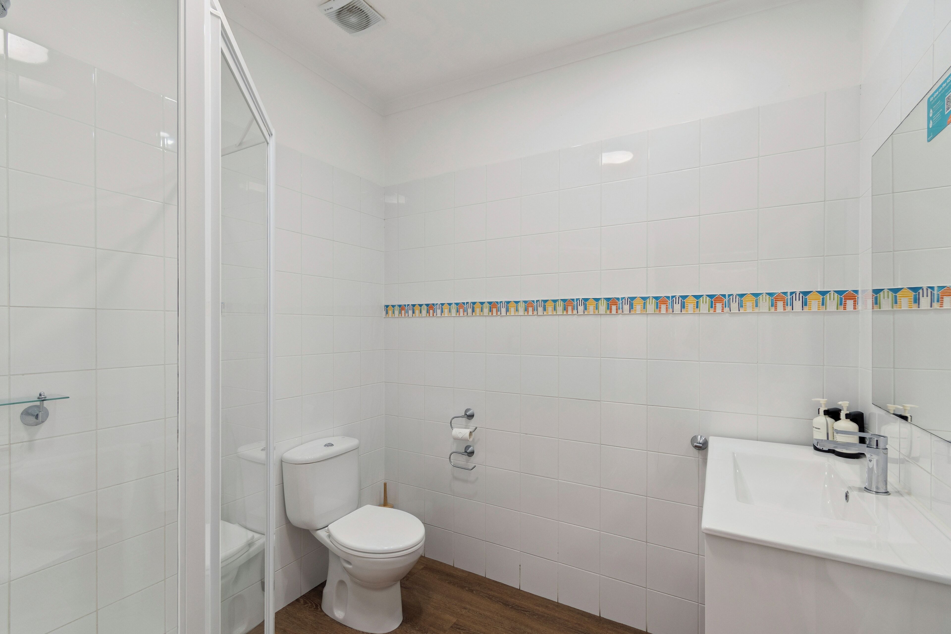 Een badkamer met witte tegels, een toilet, een wastafel en een douchegedeelte.