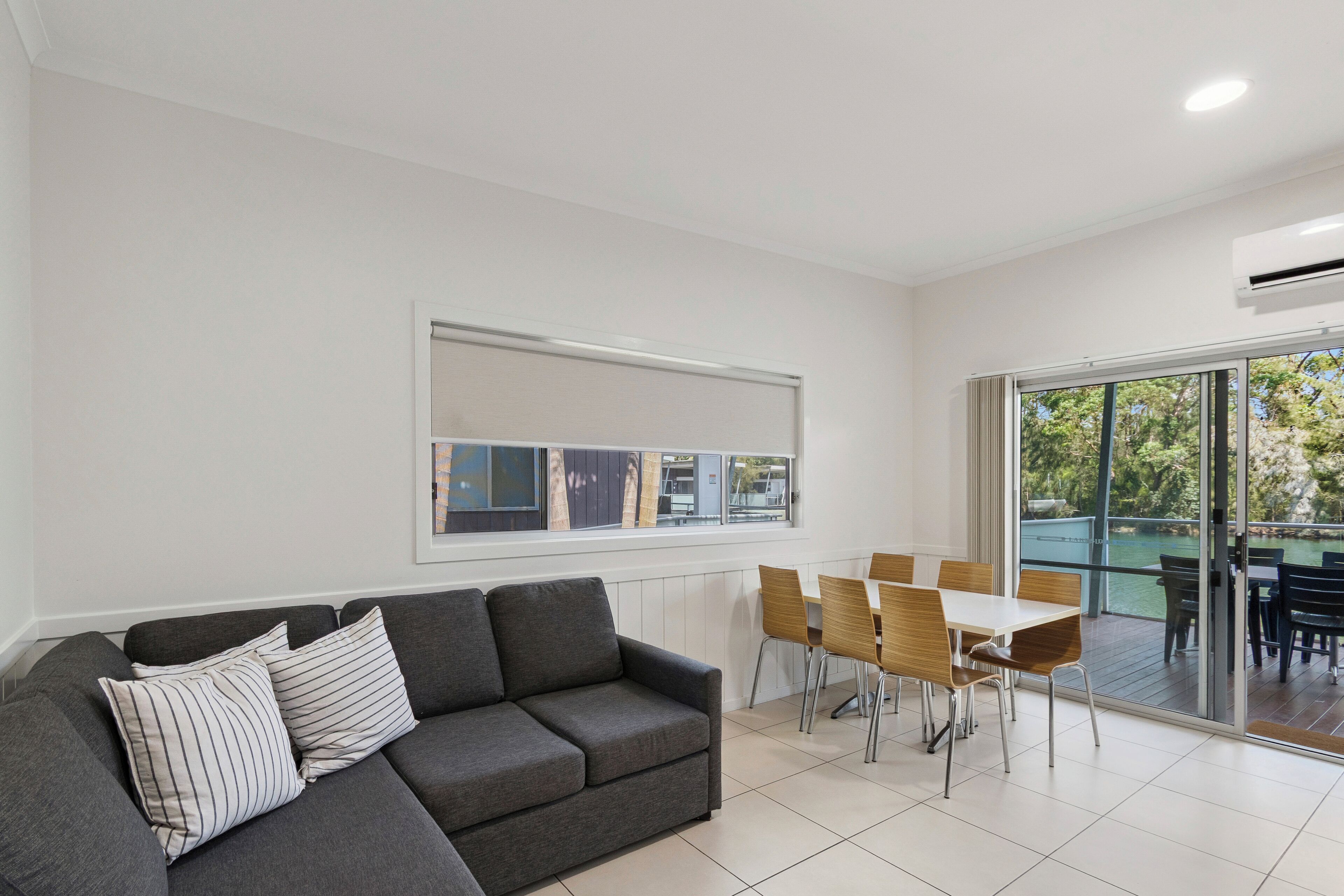 A modern living room with a grey sofa, striped pillows, a dining table with chairs, and a large window with artwork.