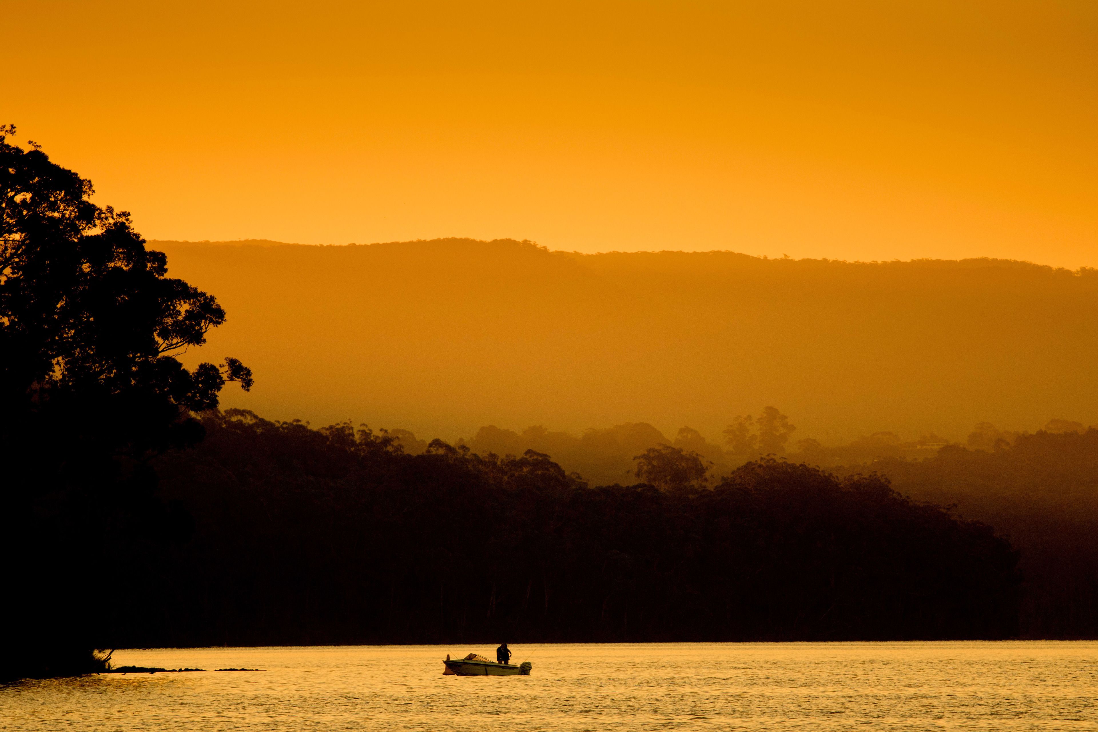 Um pôr do sol sobre águas calmas, com um barco e uma pessoa na margem.