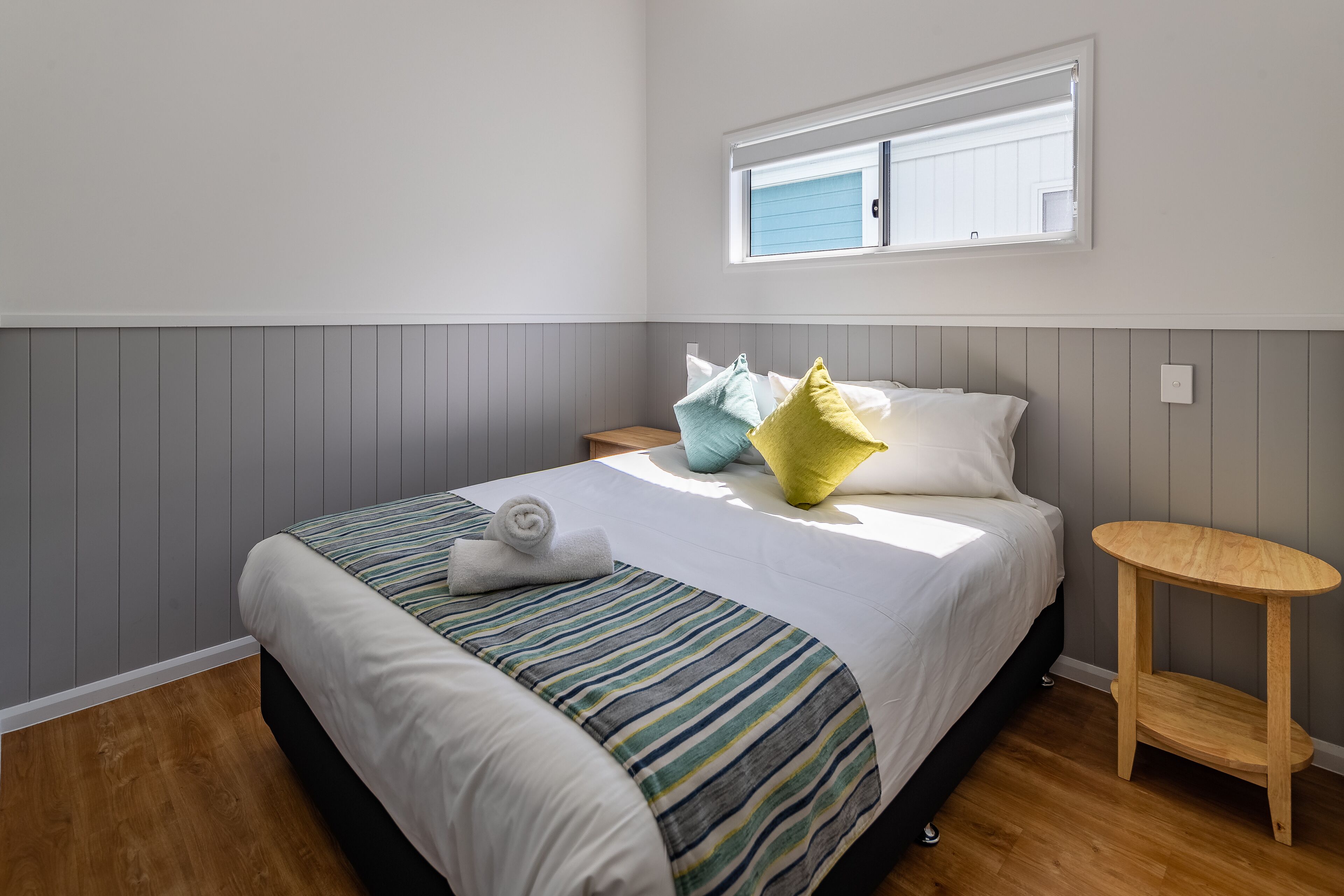 A neatly made bed with a striped bedspread, a small bedside table, and a window with blinds.