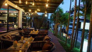 An outdoor dining area with tables and chairs, a covered walkway, and palm trees. - Apsara Residence Hotel (Siem Reap)