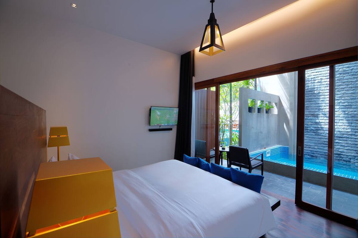 A modern hotel room with a large bed, a television, a desk, and a view of an outdoor swimming pool.
