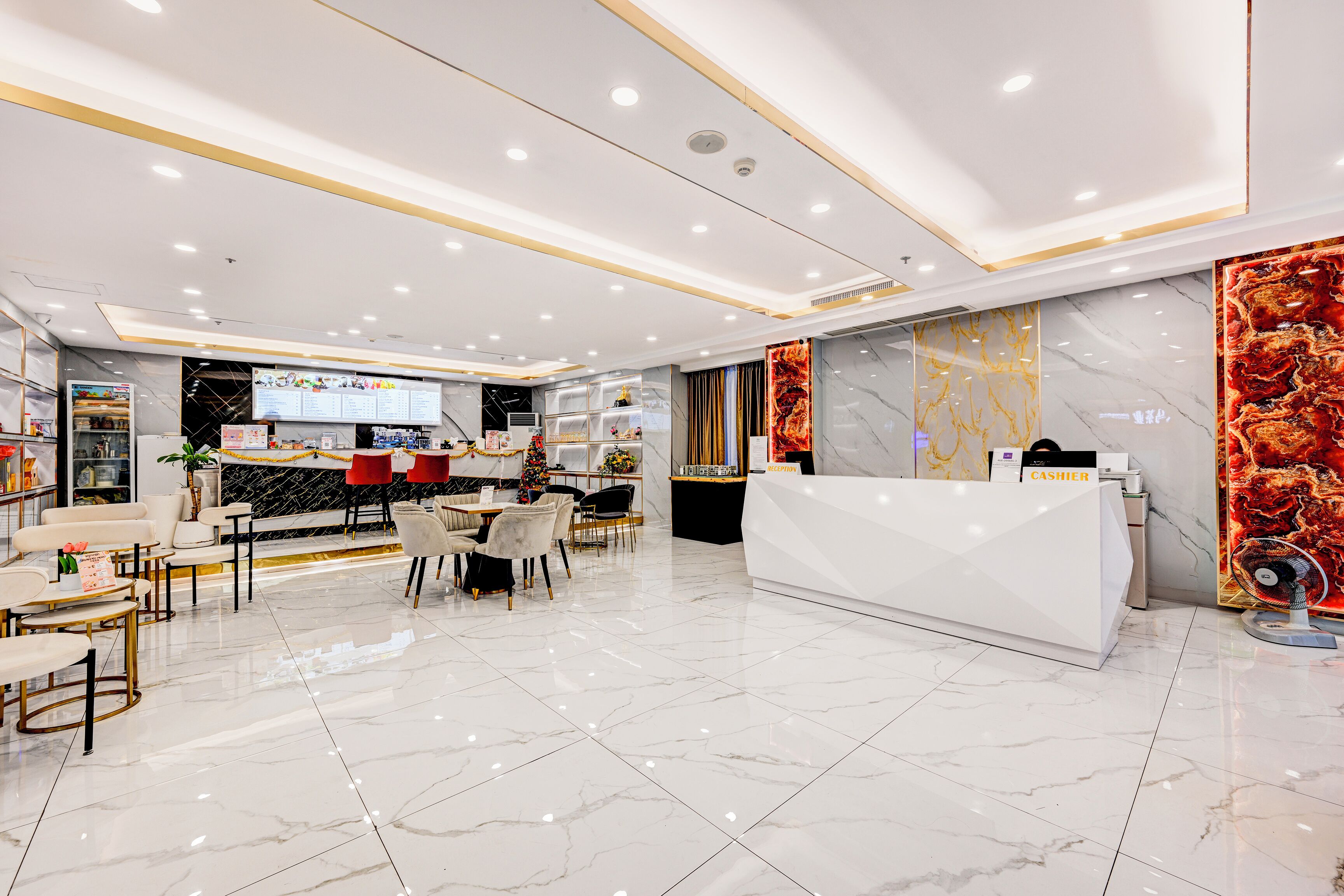 A modern hotel lobby with a white reception desk, a seating area with tables and chairs, and a large mirror wall.