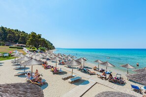 A beach with sun loungers, umbrellas, and a clear blue sea.