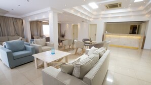 A spacious living area with a sofa, coffee table, and chairs. There is a reception desk in the background. - Elani Bay Resort (Kassandra)