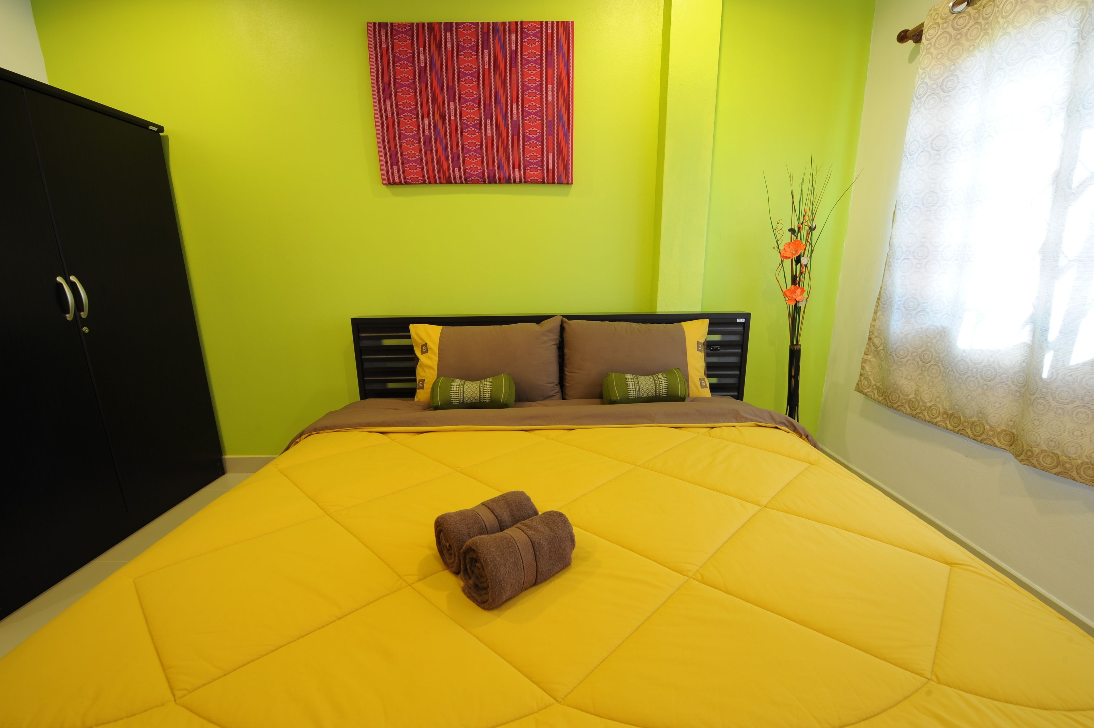 A room with a bed, green walls, a black wardrobe, and a patterned artwork.