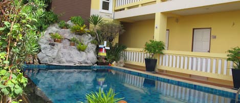 A pool area with a rock wall, potted plants, and a statue of a child.