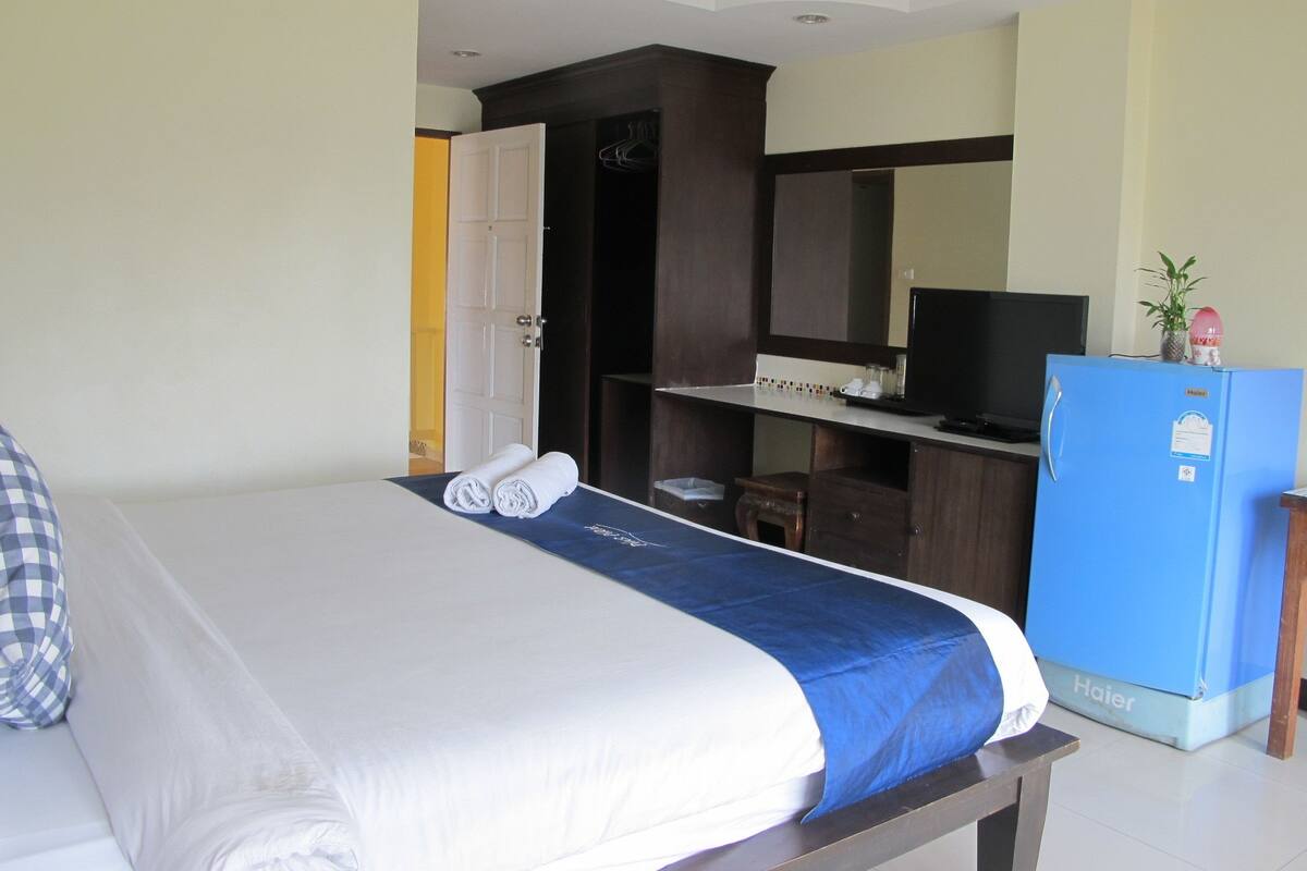 A hotel room with a bed, a desk, a television, and a refrigerator.