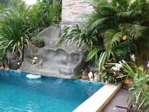 Une piscine agrémentée d’une cascade, entourée d’une végétation tropicale luxuriante.