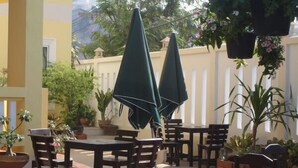 An outdoor patio with wooden tables and chairs, green umbrellas, and potted plants. - Pius Place (Pattaya)