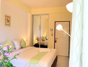 A hotel room with a bed, a mirror, a door, and a nightstand with a lamp.