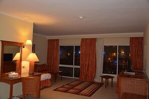 A hotel room with a large window, a sofa, a chair, a desk, and a lamp. - Le Mirage New Tiran (Sharm El Sheikh)