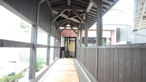A covered walkway with wooden railings and a concrete floor, leading to a building entrance. - Urayu Ryokan Urashima (Onomichi)