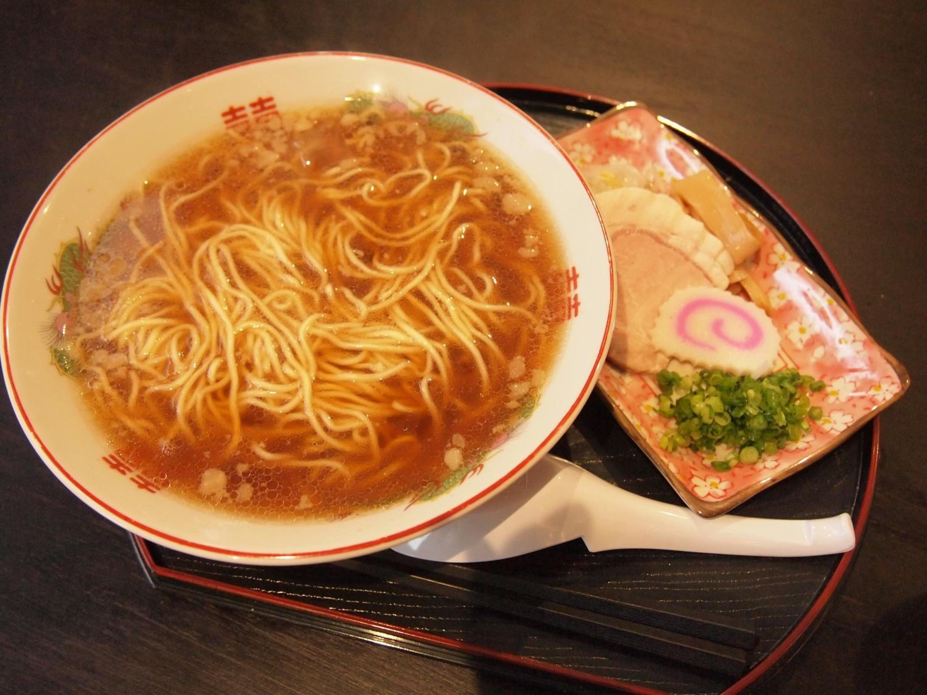 A bowl of ramen noodles in a broth with a side of sliced meat and vegetables on a tray.