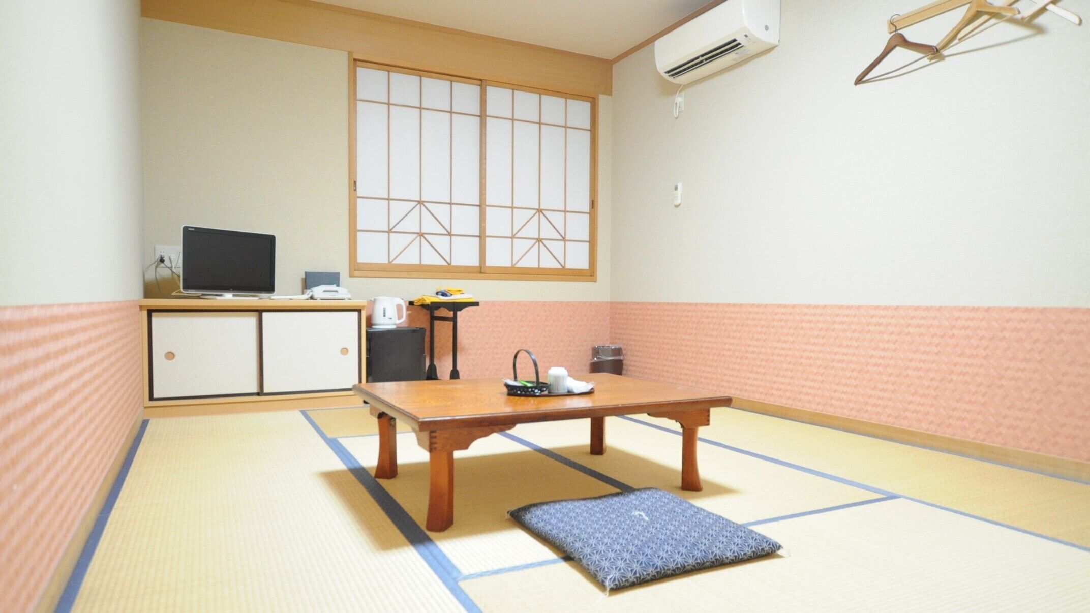 Una habitación con suelo de tatami, una mesa de madera, un televisor sobre un mueble y una ventana con diseño de cuadrícula.