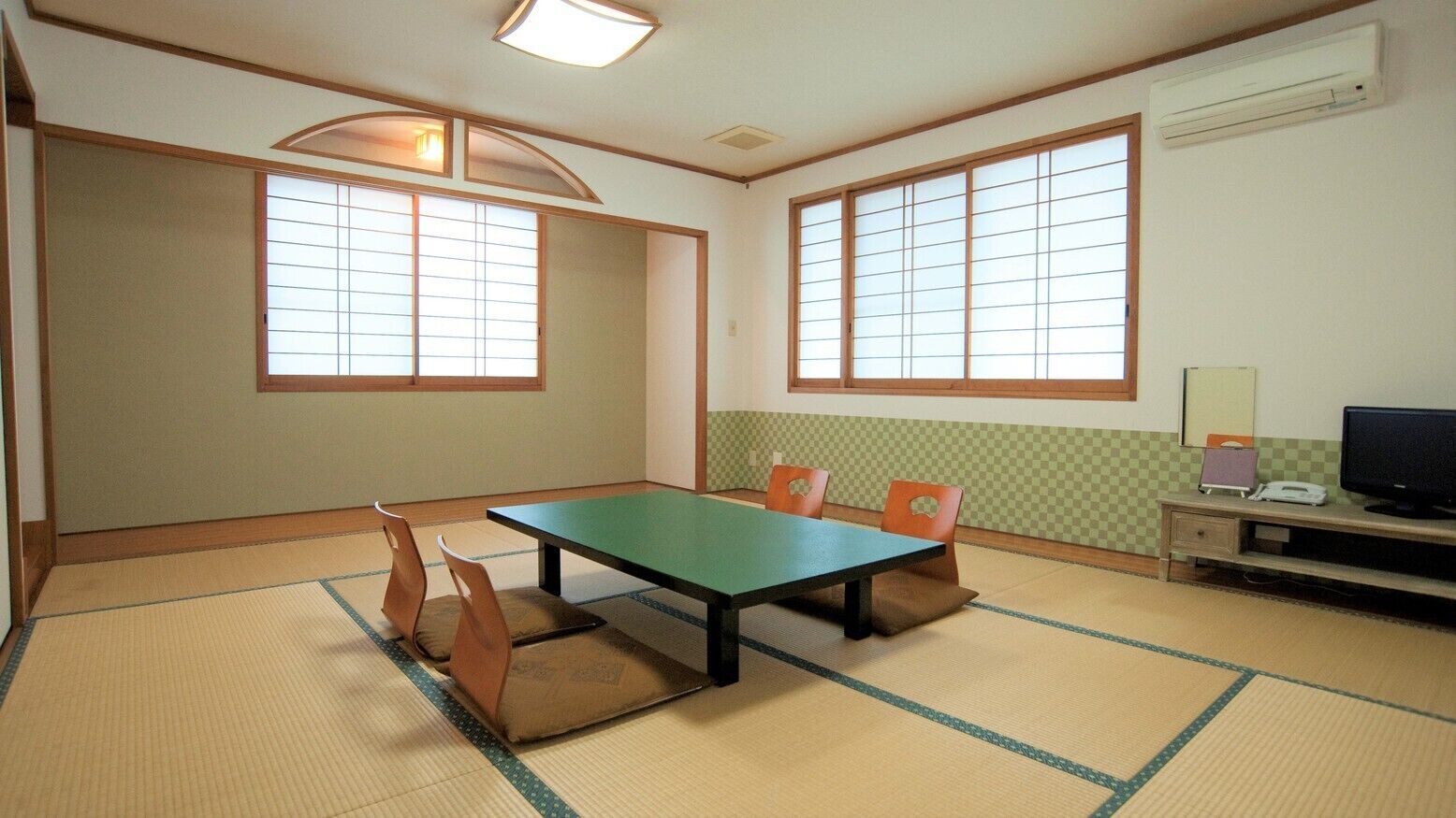 Una habitación con suelo de tatami, una mesa baja con cojines, un televisor y un pequeño escritorio con lámpara.