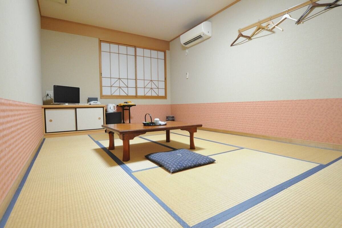 A tatami mat room with a low table, a television, and a window with shoji screens.