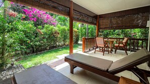 A covered outdoor seating area with a table and chairs, surrounded by lush greenery and flowering plants. - Cocotier Du Rocher (La Digue)