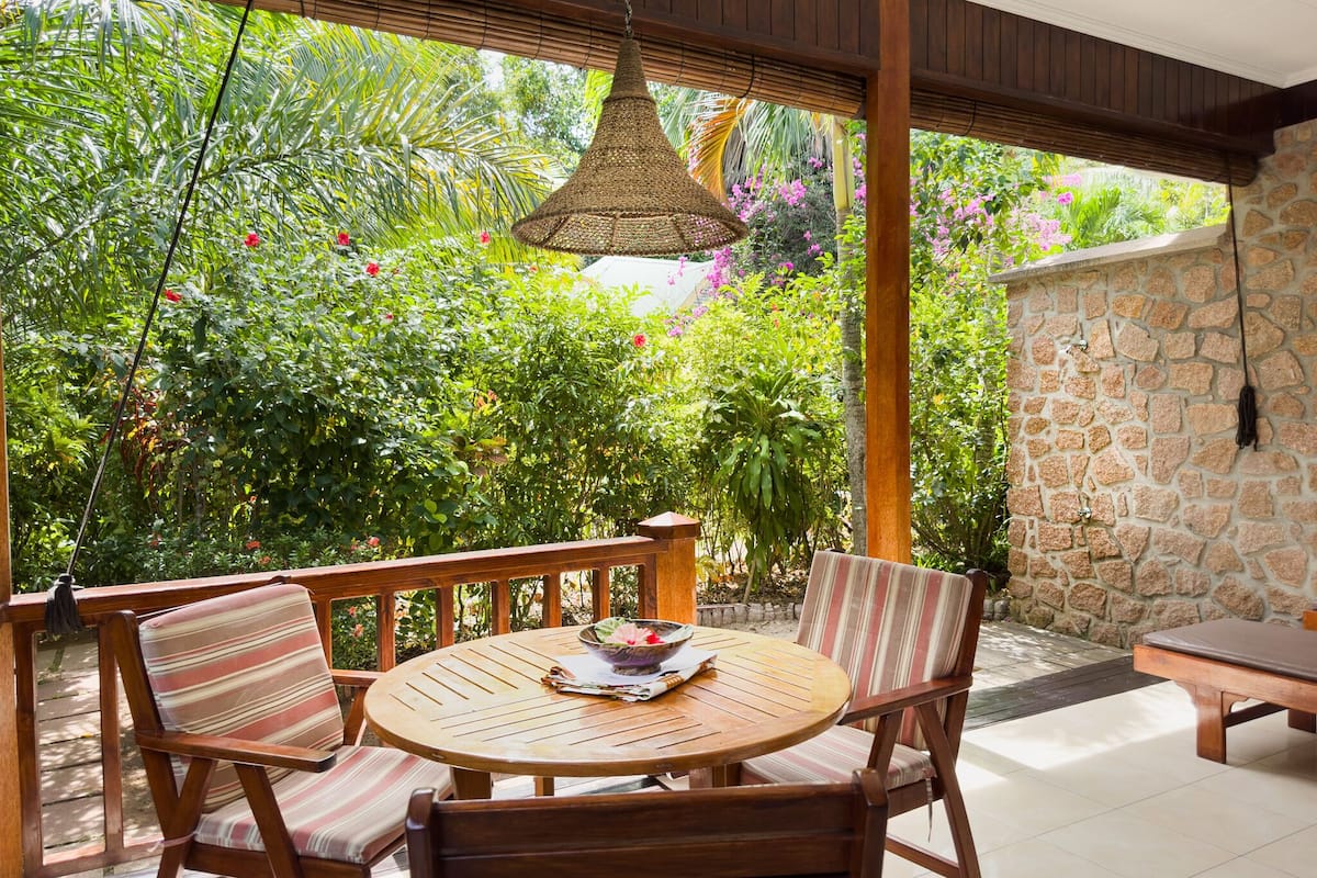 Un patio con una mesa redonda de madera, sillas con cojines a rayas y una lámpara colgante de mimbre.