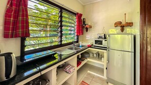 A kitchen with a window, a microwave, a refrigerator, and a sink. - Cocotier Du Rocher (La Digue)