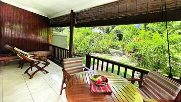 Um deck de madeira com mesa e cadeiras, uma tigela de frutas e vista para um verde exuberante.