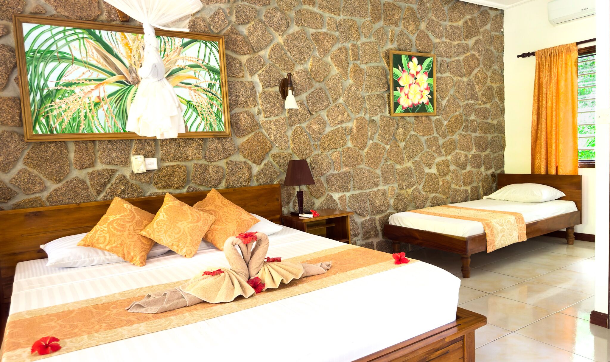 Habitación de hotel con pared de piedra, dos camas, una mesita de noche, una lámpara y obras de arte.