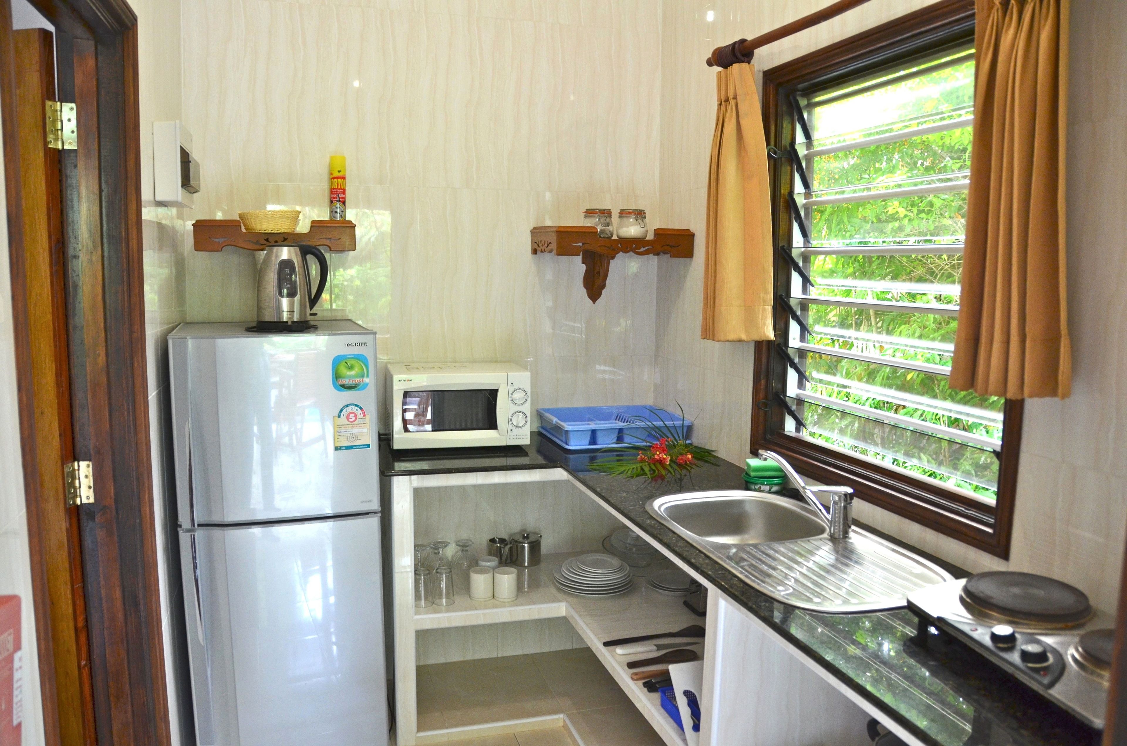 Cocina compacta con refrigerador, microondas, lavamanos y ventana con cortinas.