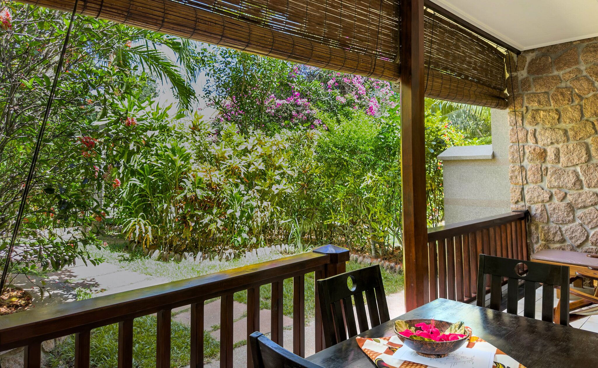 A covered patio with a stone wall, wooden railing, and a table with chairs.