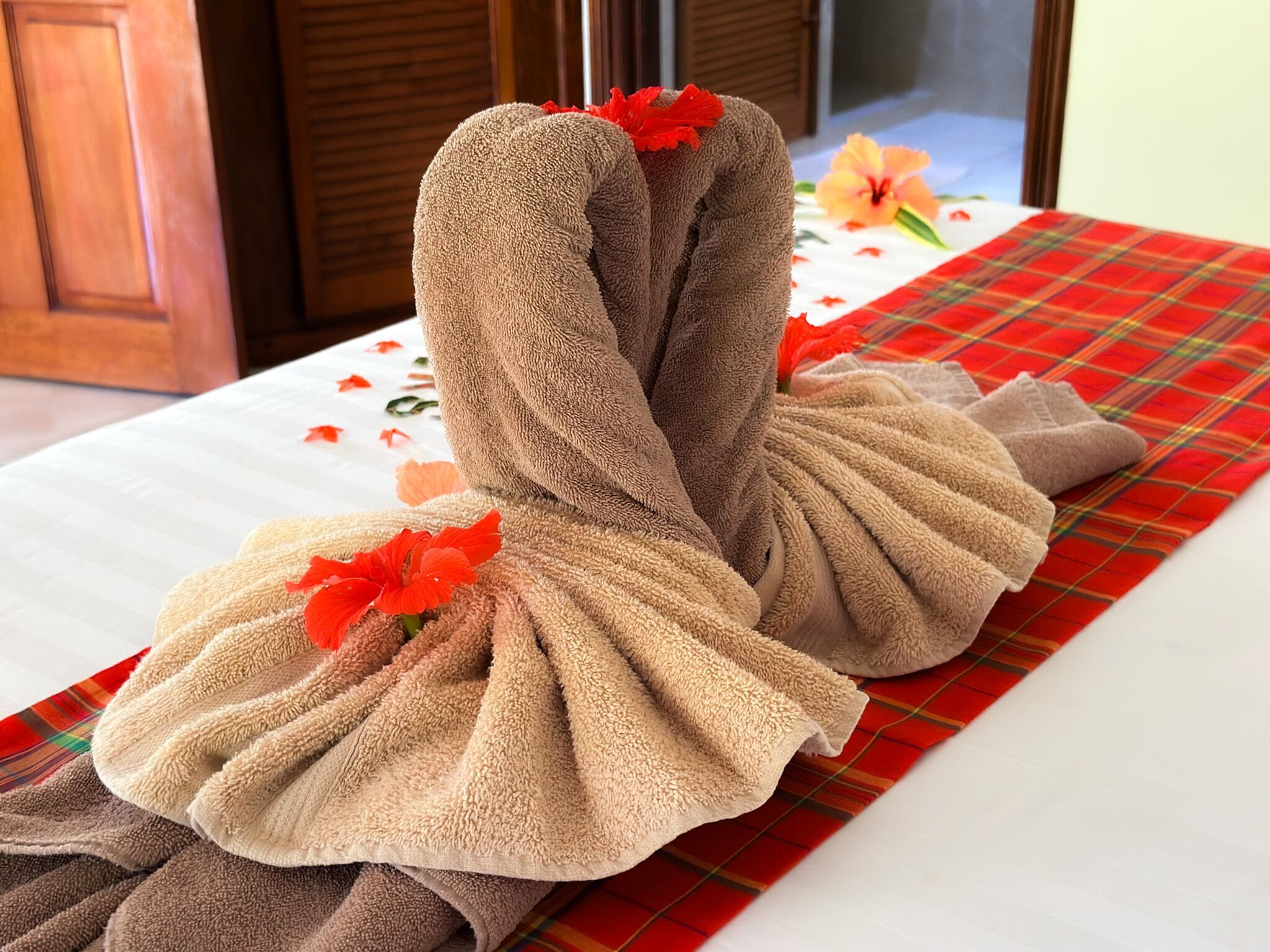 A towel arranged in a swan shape on a bed with a plaid blanket and a floral tablecloth.