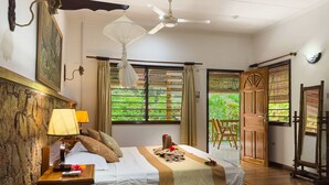 A bedroom with a bed, bedside table, lamp, and a view of greenery through the window. - Cocotier Du Rocher (La Digue)