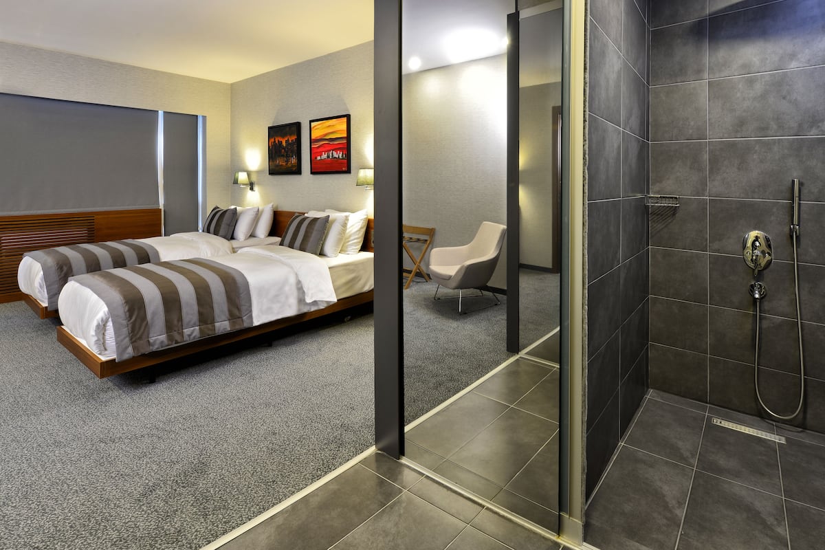 A hotel room with two beds, a shower, and a chair.