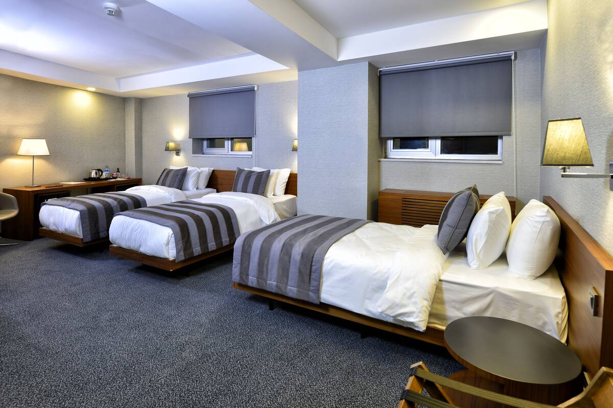 A hotel room with two beds, a desk, a chair, and a small table.