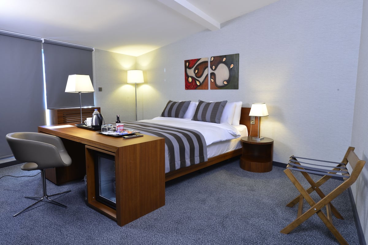 A hotel room with a bed, desk, chair, and two bedside lamps.