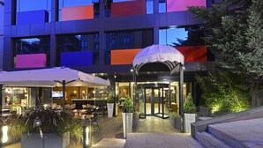 Een modern gebouw met een glazen gevel, een terras en een overdekte ingang.