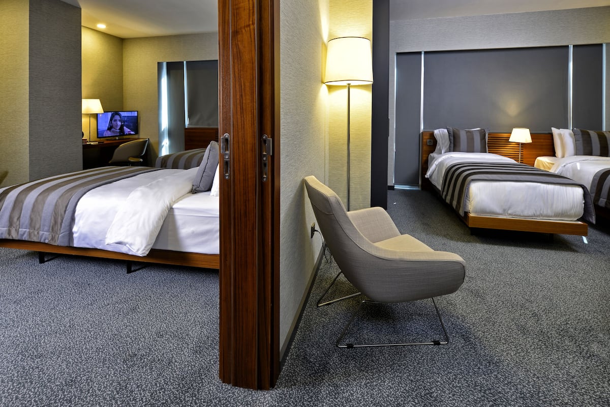 A hotel room with two beds, a desk with a TV, a chair, and a lamp.