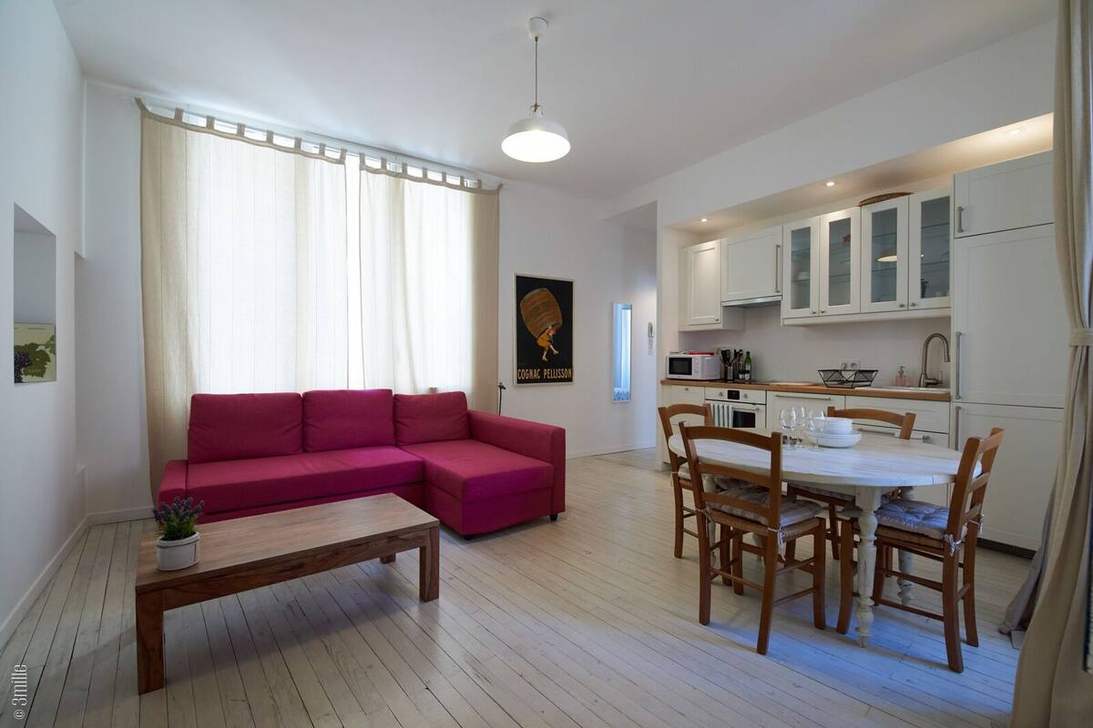 A modern apartment with a living area, a dining table with chairs, a kitchen with white cabinets, and a red sofa.