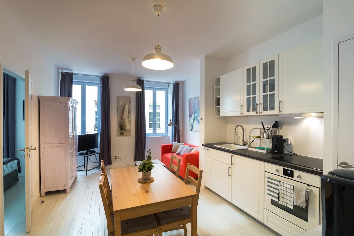 A modern kitchen with white cabinets, a wooden dining table, and a red sofa.